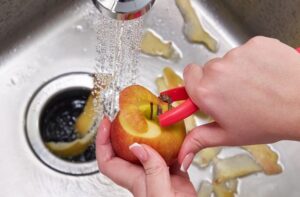 garbage disposal with running water and person peeling apple into kitchen sink