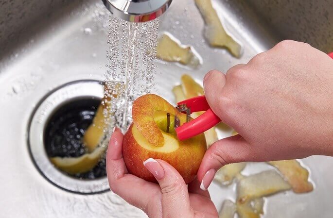 garbage disposal with running water and person peeling apple into kitchen sink